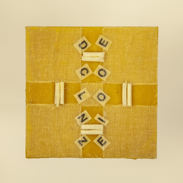 Artwork by Robin Hill that is a wooden square with beeswax, rolled cheescloth rope and letters that spell the word DECOLONIZE