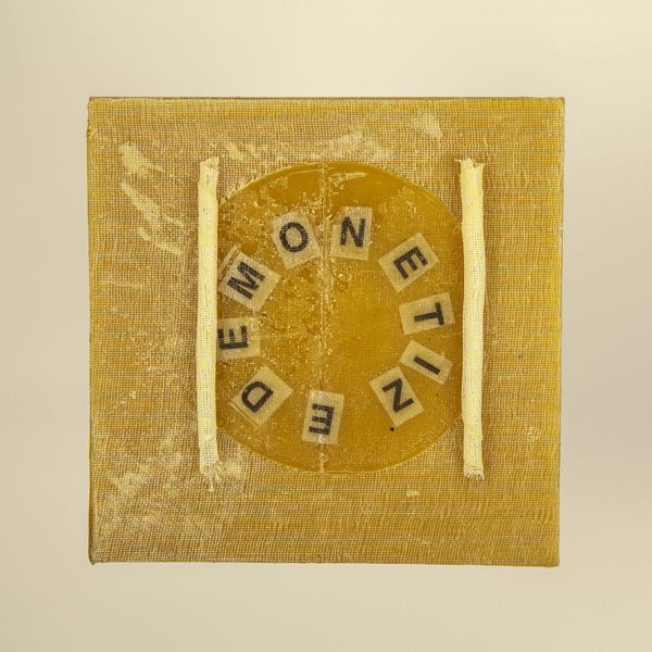 Artwork by Robin Hill that is a wooden square with beeswax, rolled cheescloth rope and letters that spell the word DEMONETIZE