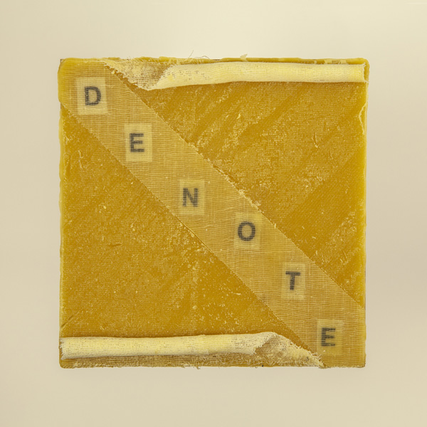 Artwork by Robin Hill that is a wooden square with beeswax, rolled cheescloth rope and letters that spell the word DENOTE