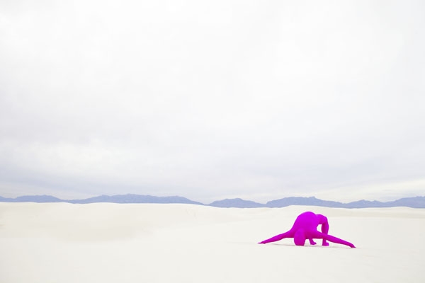 A photograph by Toban Nichols of a barren landscape with a magenta colored human form bent over backwards
