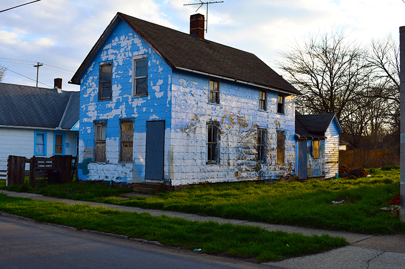 This is an image of a photograph by Vincent Johnson showing a weathered suburban home with splotchly blue paint