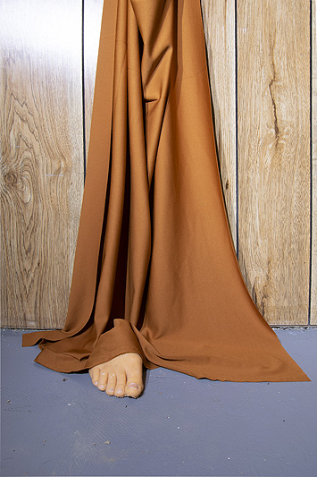 This is a picture of brown cloth hanging against a wood panel wall with a fake foot sticking out at the bottom by Richard Haley