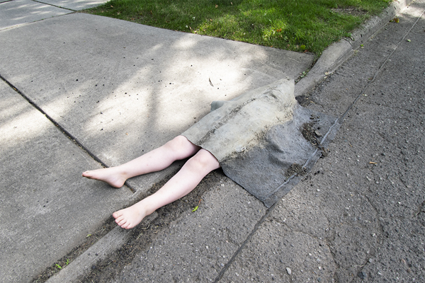This is a picture of a pair of fake human legs as they are emerging from the sidewalk and street by Richard Haley